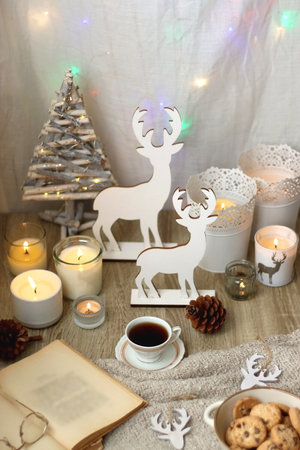 Various Christmas decorations, lit candles, cup of tea or coffee, cookies, books, presents and soft blanket on the table. Holiday hygge at home. Selective focus.の写真素材