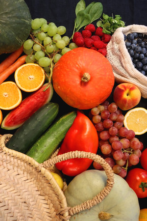 Round straw bag and various seasonal fruits and vegetables on dark background. Summer and fall produce. Top view.の写真素材