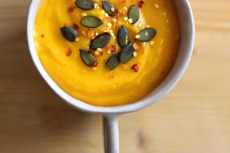 Bowl of creamy pumpkin and potato soup, with pumpkin seeds and chilli flakes toppings. Top view, wooden background.の写真素材