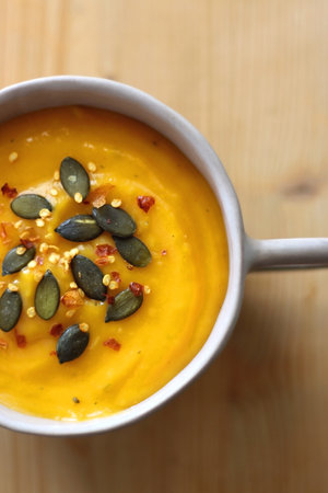 Bowl of creamy pumpkin and potato soup, with pumpkin seeds and chilli flakes toppings. Top view, wooden background.の写真素材