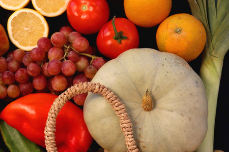 Round straw bag and various seasonal fruits and vegetables on dark background. Summer and fall produce. Top view.の写真素材