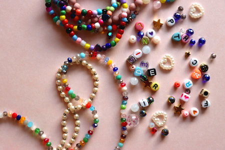 Colorful DIY necklaces, friendship bracelets and various plastic beads on pastel pink background. Flat lay.の写真素材