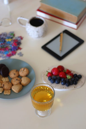Colorful jigsaw puzzle pieces, books, tablet, glasses, cookies, berries, cup of tea or coffee, glass of juice and lit candles on the table. Hygge in pastel colors. Selective focus.の写真素材