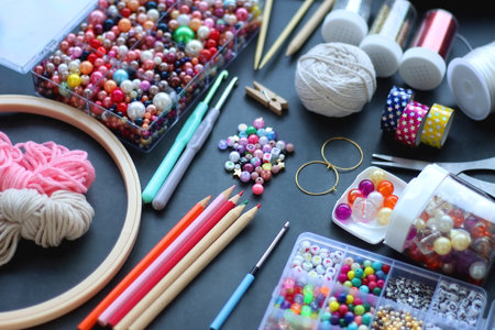 Colorful beads, coloring pencils, glitter, needles, string, hoop, tape and scissors on dark background. Various colorful craft supplies. Selective focus.の写真素材