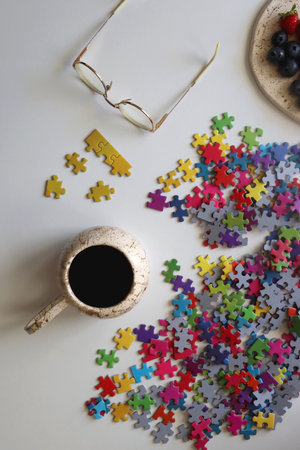 Colorful jigsaw puzzle pieces, cup of tea or coffee, eyeglasses and fresh berries for snacking. Hygge at home. Top view.の写真素材
