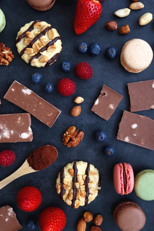 Macarons, chocolate, cookies, berries and various nuts on dark blue background. Top view.