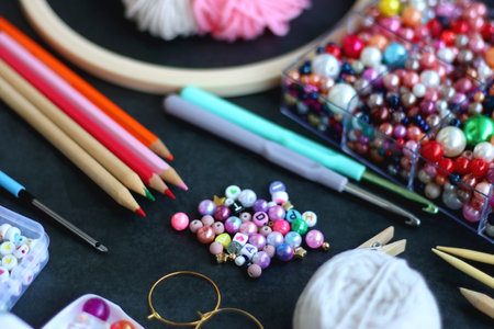 Colorful beads, coloring pencils, glitter, needles, string, hoop, tape and scissors on dark...