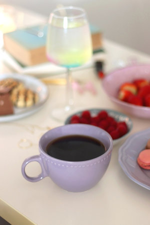 Plate of pastel macarons, cookies and chocolate, cup of tea of coffee, glass of bubble water,...