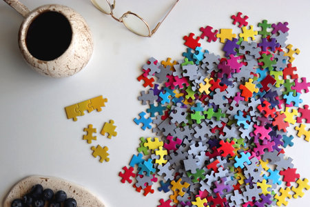 Colorful jigsaw puzzle pieces, cup of tea or coffee, eyeglasses and fresh berries for snacking. Hygge at home. Top view.の写真素材