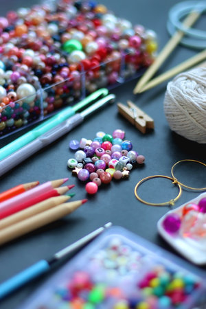 Colorful beads, coloring pencils, glitter, needles, string, hoop, tape and scissors on dark...