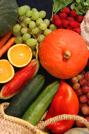 Round straw bag and various seasonal fruits and vegetables on dark background. Summer and fall produce. Top view.の写真素材