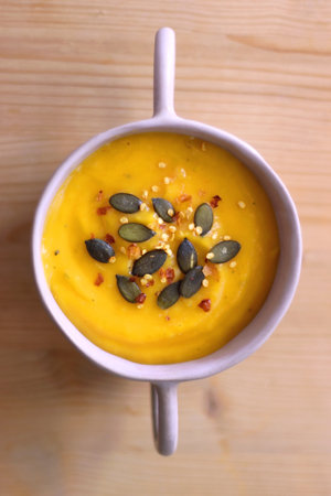Bowl of creamy pumpkin and potato soup, with pumpkin seeds and chilli flakes toppings. Top view, wooden background.の写真素材