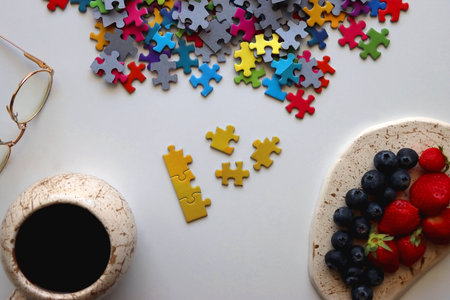 Colorful jigsaw puzzle pieces, cup of tea or coffee, eyeglasses and fresh berries for snacking....