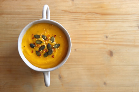 Bowl of creamy pumpkin and potato soup, with pumpkin seeds and chilli flakes toppings. Top view, wooden background.の写真素材