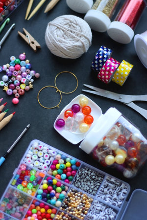 Colorful beads, coloring pencils, glitter, needles, string, hoop, tape and scissors on dark background. Various colorful craft supplies. Selective focus.の写真素材