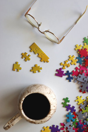 Colorful jigsaw puzzle pieces, cup of tea or coffee, eyeglasses and fresh berries for snacking. Top view.の写真素材