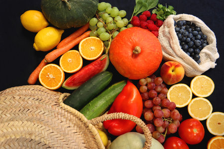 Round straw bag and various seasonal fruits and vegetables on dark background. Summer and fall...