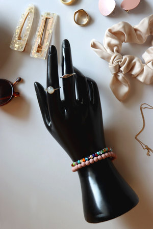 Hand figurine, sunglasses, gold jewelry, colorful bead jewelry, statement rings and various hair accessories on the white table. Flat lay.の写真素材
