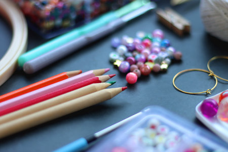 Colorful beads, coloring pencils, glitter, needles, string, hoop, tape and scissors on dark background. Various colorful craft supplies. Selective focus.の写真素材