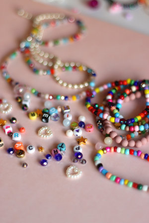 Colorful DIY necklaces, friendship bracelets and various plastic beads on pastel pink background. Selective focus.の写真素材