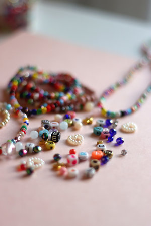 Colorful DIY necklaces, friendship bracelets and various plastic beads on pastel pink background. Selective focus.の写真素材