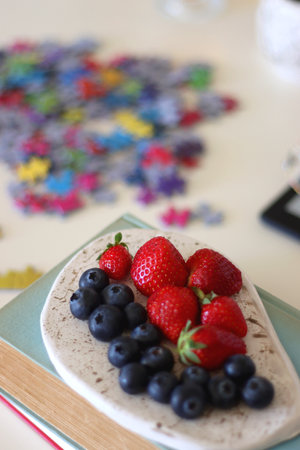 Colorful jigsaw puzzle pieces, books, tablet, glasses, cookies, berries, cup of tea or coffee, glass of juice and lit candles on the table. Hygge in pastel colors. Selective focus.の写真素材