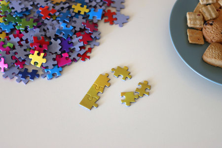 Colorful jigsaw puzzle pieces, books, tablet, glasses, cookies, berries, cup of tea or coffee, glass of juice and lit candles on the table. Hygge in pastel colors. Selective focus.の写真素材