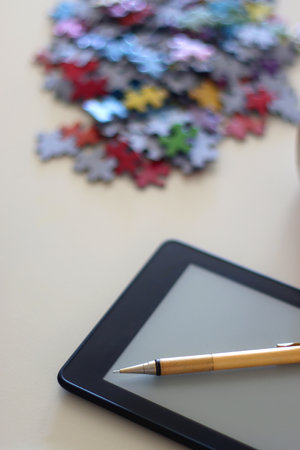 Colorful jigsaw puzzle pieces, books, tablet, glasses, cookies, berries, cup of tea or coffee, glass of juice and lit candles on the table. Selective focus.の写真素材