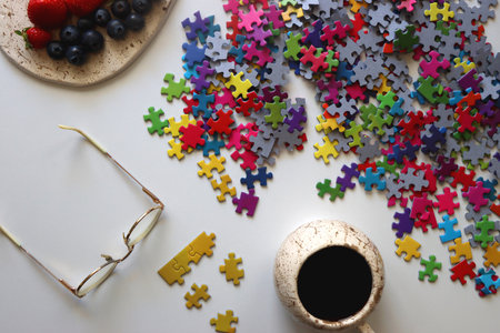 Colorful jigsaw puzzle pieces, cup of tea or coffee, eyeglasses and fresh berries for snacking. Hygge at home. Top view.の写真素材