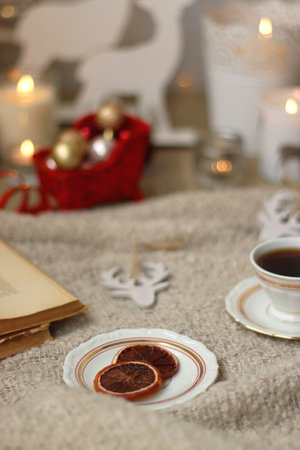 Various Christmas decorations, lit candles, cup of tea or coffee, cookies, books, presents and soft blanket on the table. Holiday hygge at home. Selective focus.の写真素材