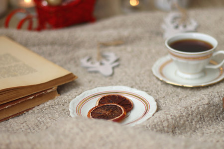Various Christmas decorations, lit candles, cup of tea or coffee, cookies, books, presents and soft blanket on the table. Holiday hygge at home. Selective focus.の写真素材