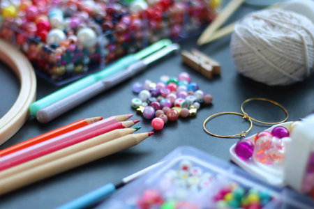 Colorful beads, coloring pencils, glitter, needles, string, hoop, tape and scissors on dark background. Various colorful craft supplies. Selective focus.の写真素材