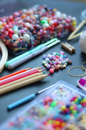 Colorful beads, coloring pencils, glitter, needles, string, hoop, tape and scissors on dark background. Various colorful craft supplies. Selective focus.の写真素材