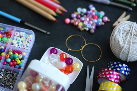 Colorful beads, coloring pencils, glitter, needles, string, hoop, tape and scissors on dark...