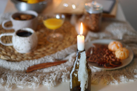 Books, e-reader, tea, orange juice, fruit, snacks, yarn, blanket and lit candles on the table. Autumn or winter hygge at home. Selective focus.の写真素材