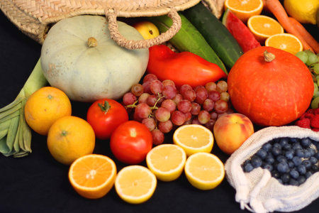 Round straw bag and various seasonal fruits and vegetables on dark background. Summer and fall produce. Selective focus.の写真素材