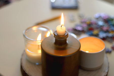 Colorful jigsaw puzzle pieces, books, tablet, glasses, cookies, berries, cup of tea or coffee, glass of juice and lit candles on the table. Hygge in pastel colors. Selective focus.の写真素材