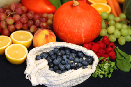Round straw bag and various seasonal fruits and vegetables on dark background. Summer and fall produce. Selective focus.の写真素材