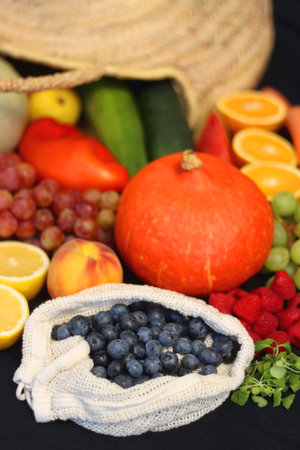 Round straw bag and various seasonal fruits and vegetables on dark background. Summer and fall produce. Selective focus.の写真素材