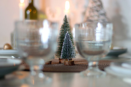 Table set for Christmas meal with plates, glasses, holiday decorations, lit candles and wine. Selective focus.の写真素材