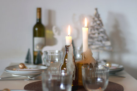 Table set for Christmas meal with plates, glasses, holiday decorations, lit candles and wine. Selective focus.の写真素材