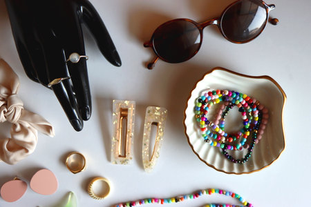 Hand figurine, sunglasses, gold jewelry, colorful bead jewelry, statement rings and various hair accessories on the white table. Flat lay.の写真素材