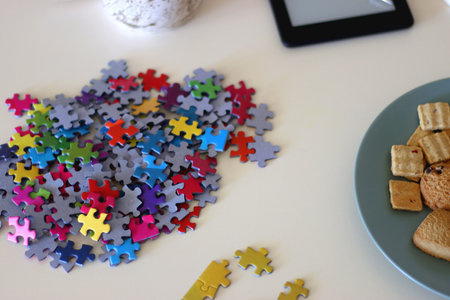 Colorful jigsaw puzzle pieces, books, tablet, glasses, cookies, berries, cup of tea or coffee, glass of juice and lit candles on the table. Hygge in pastel colors. Selective focus.の写真素材
