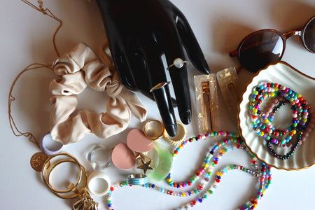 Hand figurine, sunglasses, gold jewelry, colorful bead jewelry, statement rings and various hair accessories on the white table. Flat lay.の写真素材