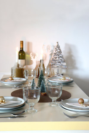 Table set for Christmas meal with plates, glasses, holiday decorations, lit candles and wine. Selective focus.の写真素材