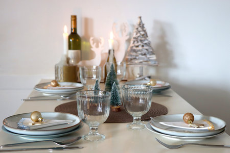 Table set for Christmas meal with plates, glasses, holiday decorations, lit candles and wine. Selective focus.の写真素材