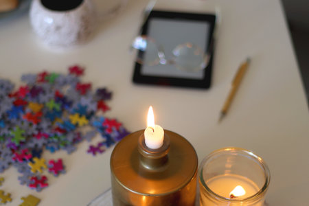 Colorful jigsaw puzzle pieces, books, tablet, glasses, cookies, berries, cup of tea or coffee, glass of juice and lit candles on the table. Hygge in pastel colors. Selective focus.の写真素材