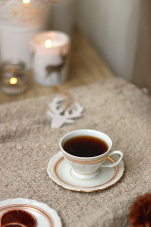 Various Christmas decorations, lit candles, cup of tea or coffee, cookies, books, presents and soft blanket on the table. Holiday hygge at home. Selective focus.の写真素材