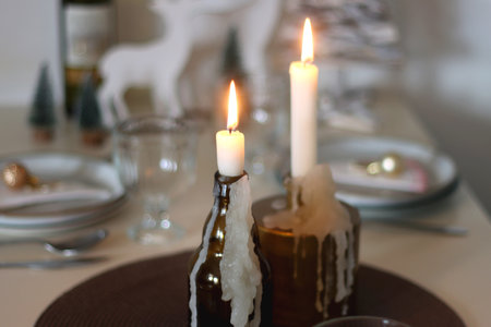 Table set for Christmas meal with plates, glasses, holiday decorations, lit candles and wine. Selective focus.の写真素材