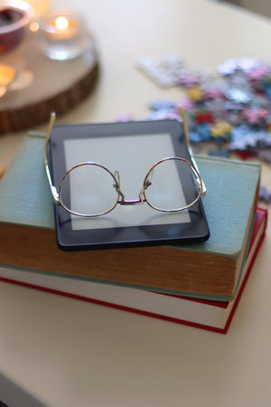 Colorful jigsaw puzzle pieces, books, tablet, glasses, cookies, berries, cup of tea or coffee, glass of juice and lit candles on the table. Hygge in pastel colors. Selective focus.の写真素材